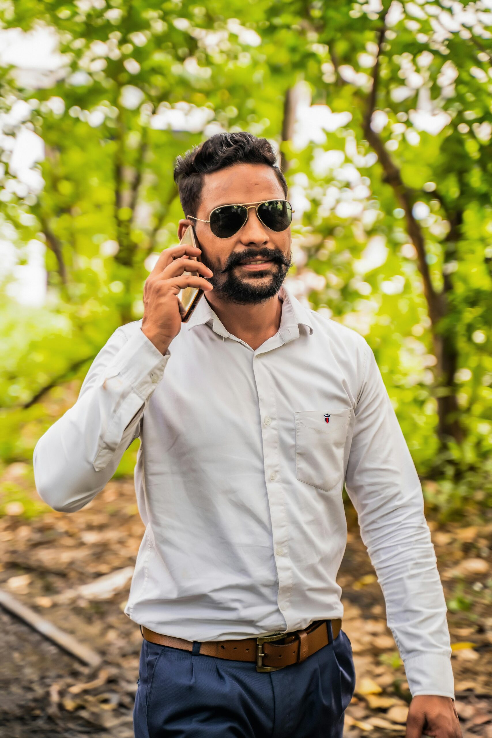 Confident man in white dress shirt talks on phone while walking outside.